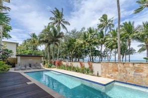 A swimming pool with lounge chairs, palm trees, and a stone wall.