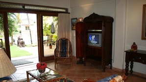 Uma sala de estar com televisão, sofá, poltrona e uma mesa com um vaso.