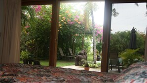 Quarto com cama, vista para um jardim com estátua e área de pátio com cadeiras e mesa.