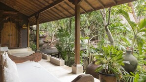 A covered outdoor seating area with a wooden bench and a stone planter. - Citrus Tree Villas - Layla (Legian)