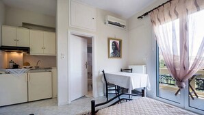 Ein gemütlicher Raum mit Bett, Esstisch mit Stühlen, einer Küchenzeile und einem großen Fenster mit Vorhängen.