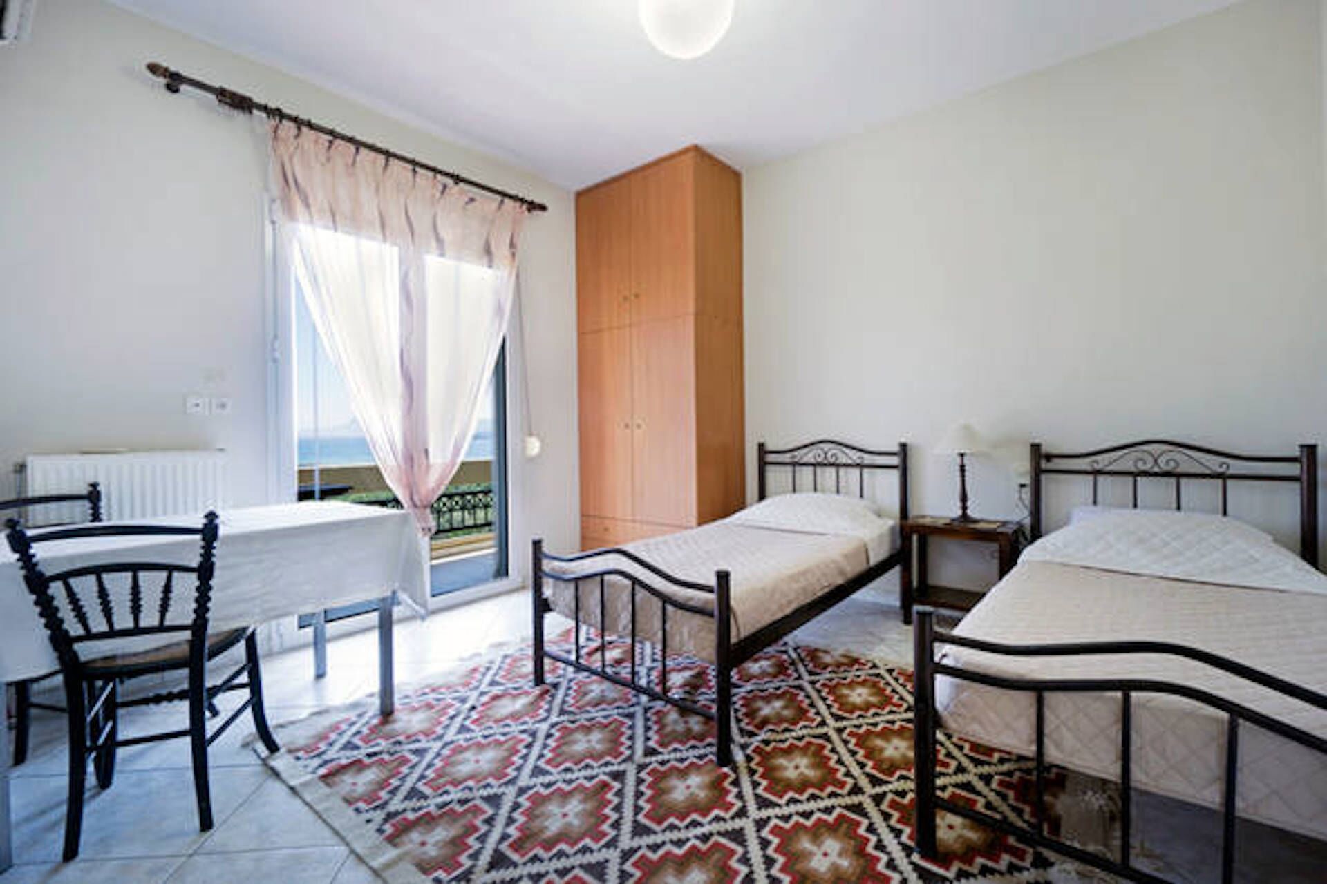 Ein Schlafzimmer mit Bett, Stuhl, Tisch und einem Fenster mit Vorhängen.