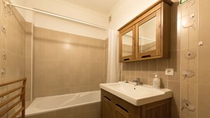 Ein Badezimmer mit einer Badewanne, einem Holzkosmetikschrank mit Spiegel und beigen Fliesen.