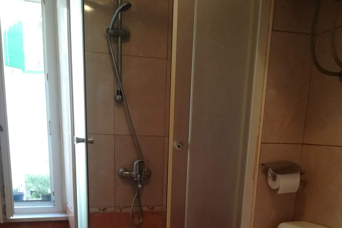 Un baño con ducha de vidrio, inodoro y una ventana pequeña.