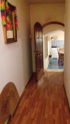 A hallway with wooden flooring, a door leading to a room, and a mirror on the wall.