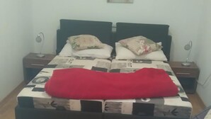 A bedroom with a bed, a nightstand, a bedside table, a chair, and a wall-mounted artwork. - Inchy Accommodation (Split)