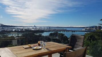 A wooden table with chairs on a balcony overlooking a marina with boats and a bridge in the distance.
