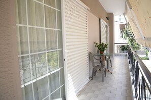 Enjoy the serene views from this balcony with a glass table and two chairs, surrounded by lush greenery.