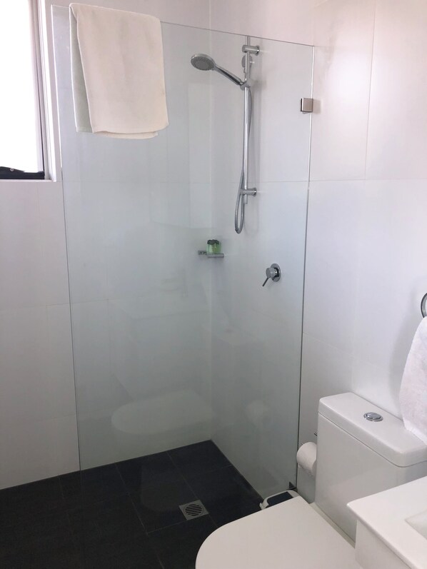 A modern bathroom with a glass-enclosed shower, a white toilet, and a sink. - BONDI BEACH STUDIOS: X (Bondi)