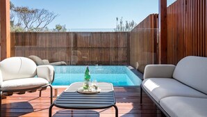 Un'area piscina con un prendisole di legno, due divani bianchi e un tavolo con una bottiglia e dei bicchieri.