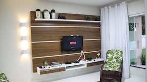 Uma sala de estar com uma estante de madeira, uma televisão de tela plana e uma poltrona de vime.