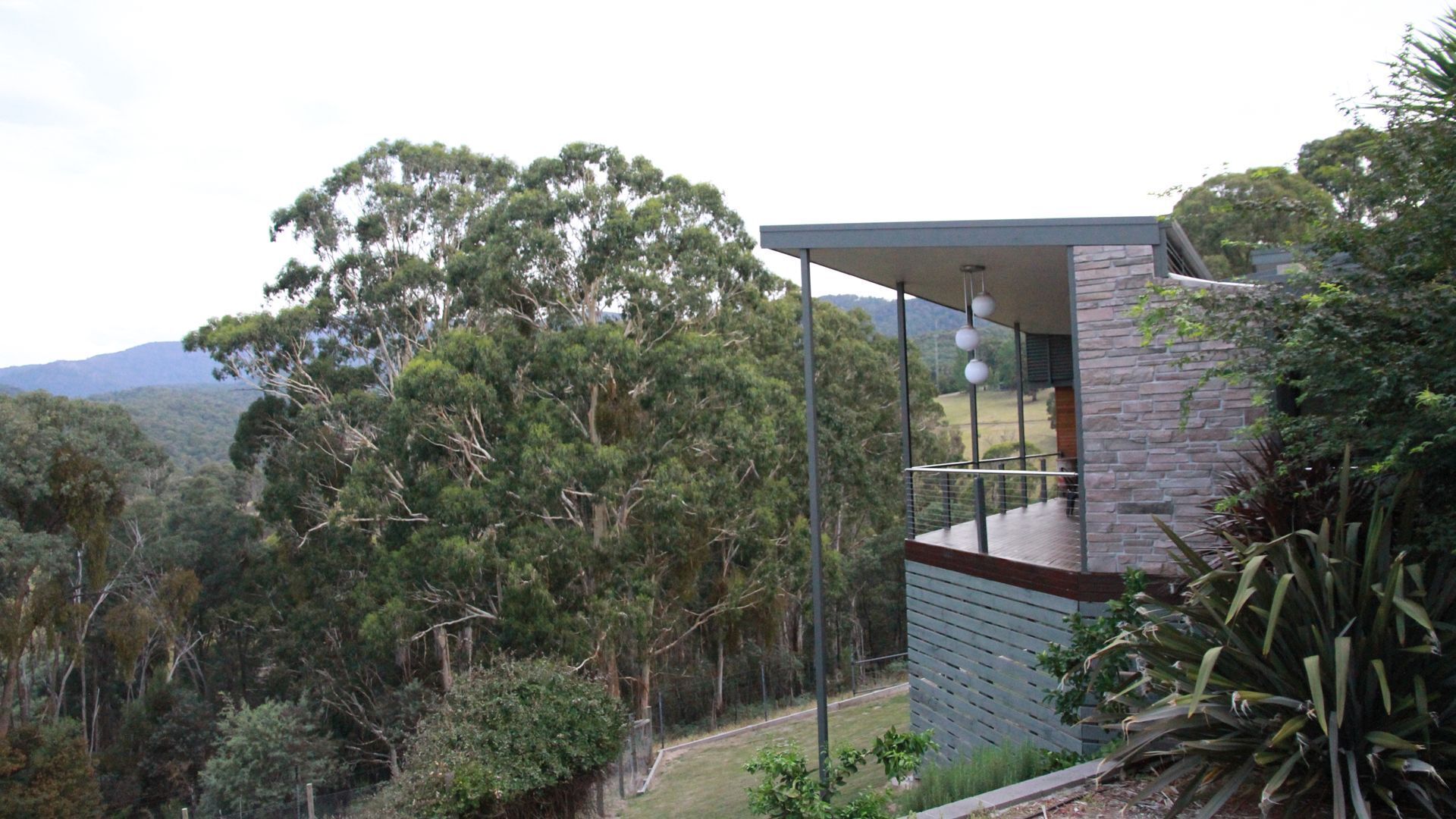A modern house with a balcony overlooking a forested area.
