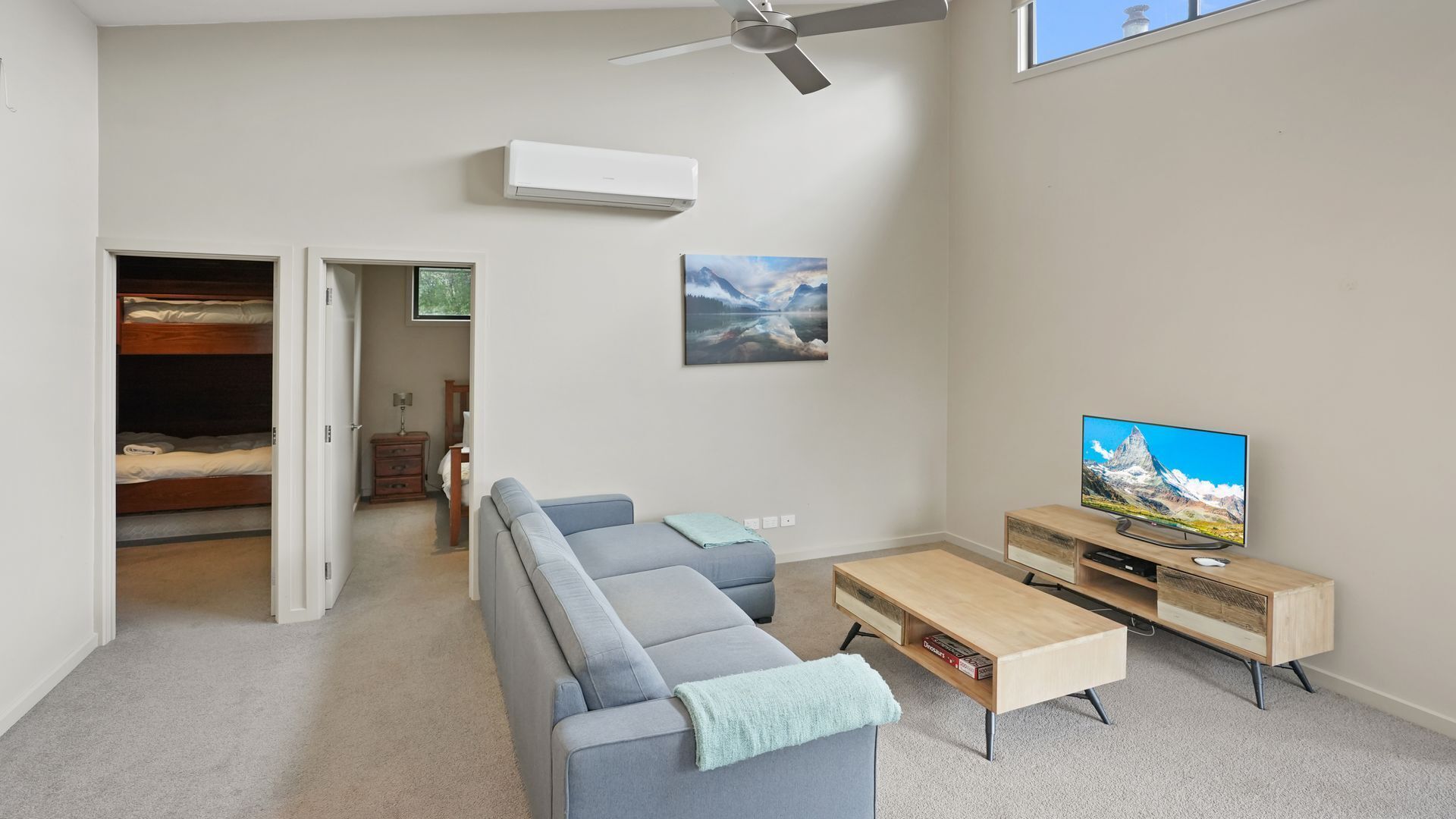 Una sala de estar moderna con un sofá gris, una mesa de centro de madera, un televisor sobre un mueble de madera y un ventilador de techo.