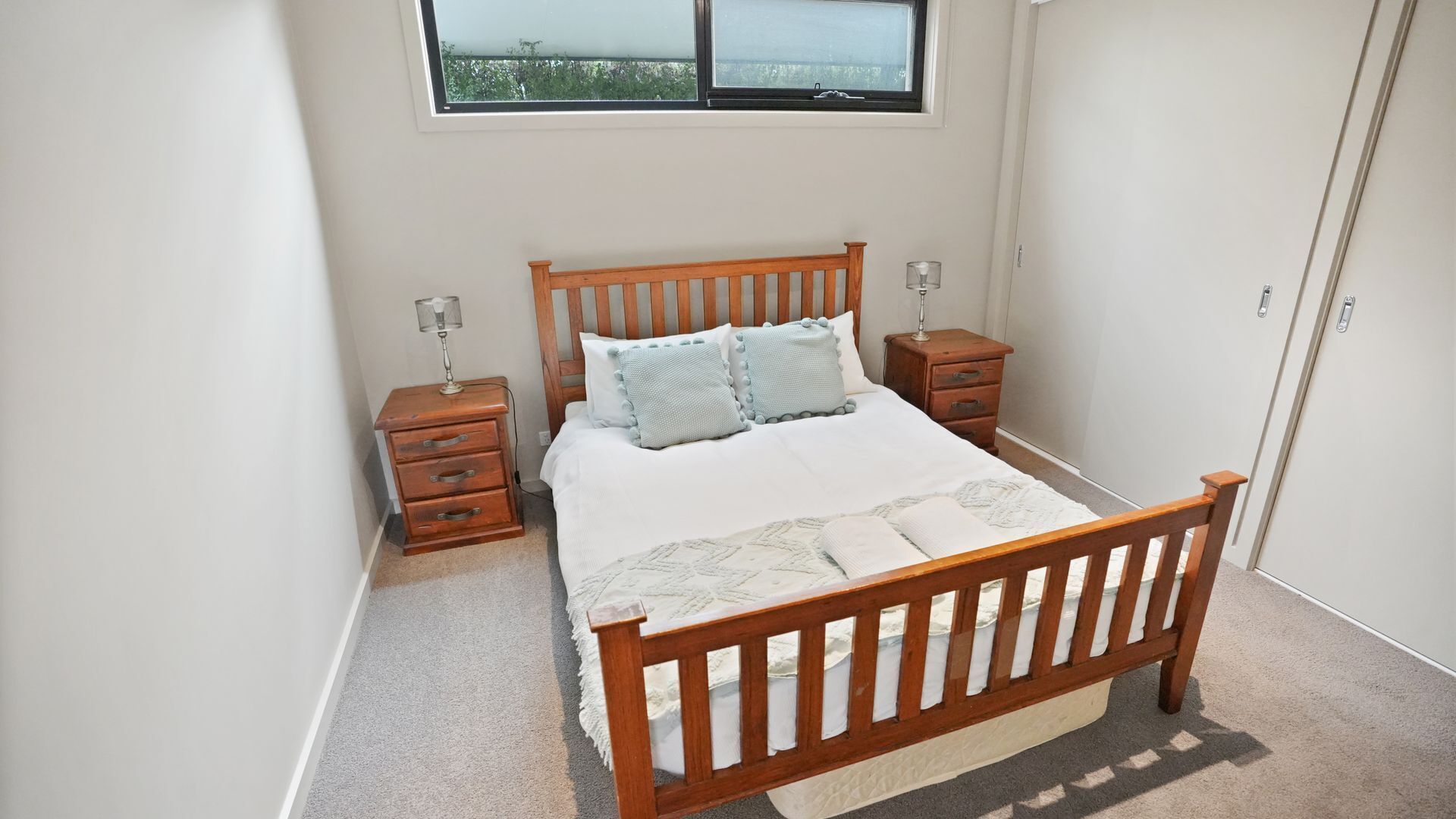 A bedroom with a wooden bed, two bedside tables, a nightstand, and a window with a view.