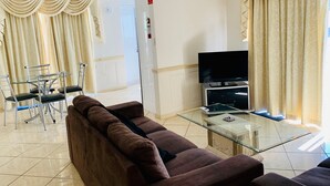 A living room with a glass coffee table, a brown sofa, a TV, and curtains. - "Redcliffe Villa" - Redcliffe Q 4020 (Redcliffe)