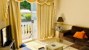 A living room with a glass coffee table, a brown sofa with an orange pillow, a TV, and a lamp on a glass table. - "Redcliffe Villa" - Redcliffe Q 4020 (Redcliffe)