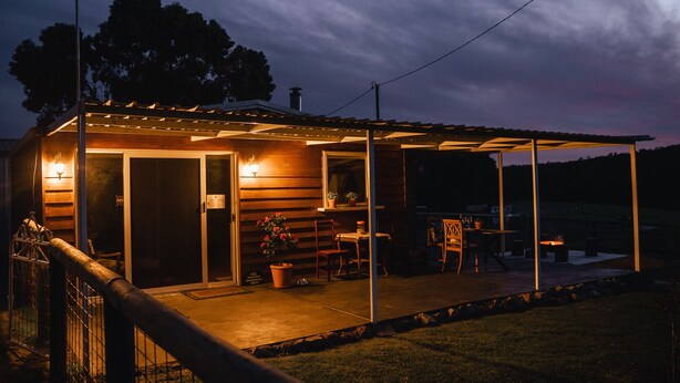 A wooden cabin with a covered patio, a door with a sign, and a small table with chairs. - Charming Rural Escape in Mumballup - Views, Fire Pit, Walks & Pet-Friendly Stay (Mumballup)