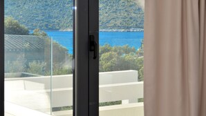 Une vue depuis une fenêtre avec une porte, donnant sur une étendue d’eau et un paysage vallonné.