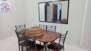 Un comedor con una mesa de madera y seis sillas, un mantel tejido decorativo, un reloj y un espejo enmarcado en la pared.