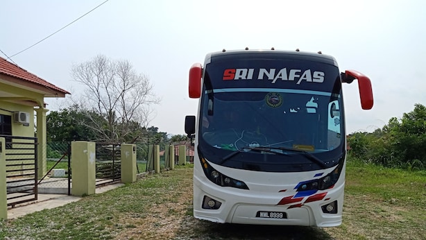 Un autobús blanco con la marca 'Sri Nafas' estacionado sobre un camino de grava.