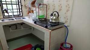 Una cocina con estufa a gas, hervidor, escurreplatos y cilindro de gas.