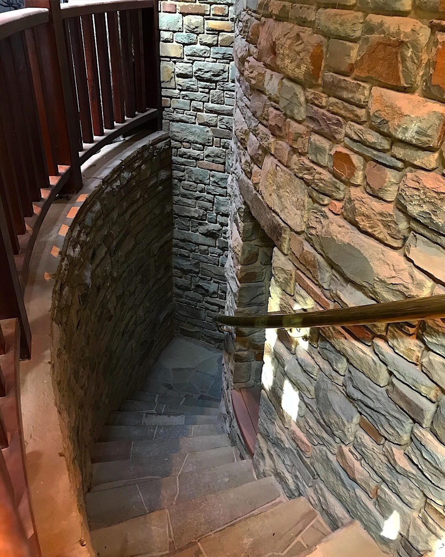 A stone staircase with a wooden handrail and a wooden railing on the left.