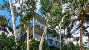 Un immeuble moderne à plusieurs étages, doté de balcons, entouré d’une végétation luxuriante et d’arbres imposants.