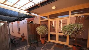 A covered patio area with stone flooring, two potted plants, a chair, and a table. - Friendly meeting chapel (North Adelaide)