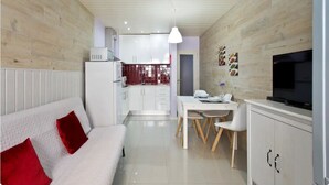 Een moderne keuken met witte kastjes, een eettafel met stoelen en een televisie rechts.