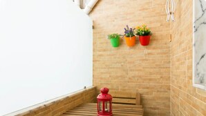 Een houten bank met een rode lantaarn, planten in potten en een bakstenen muur.