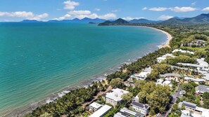 An aerial view of a coastal area with a beach, residential buildings, and mountains in the distance.