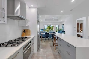 A modern kitchen with a central island, a dining area with chairs, and a view of the outdoors.