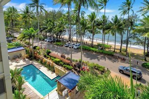 A pool, palm trees, a beach, and parked cars.
