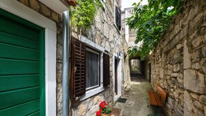Un estrecho callejón con paredes de piedra, una puerta verde y plantas en macetas.