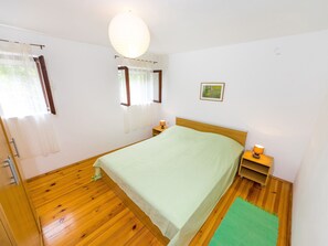 Un dormitorio con suelo de madera, una cama con cubrecama verde, dos lámparas de noche y un ventanal con cortinas.