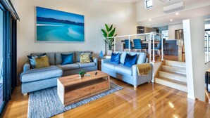 A modern living room with a large painting, two sofas, a coffee table, and a staircase leading to a dining area. - Shorelines 26, Seaview Apartment on Hamilton Island (Hamilton Island)