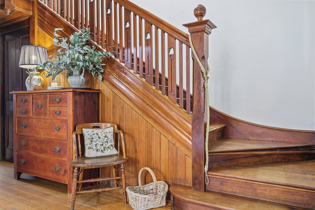 A wooden staircase with a handrail, a wooden chair with a cushion, a wicker basket, and a wooden dresser with drawers.