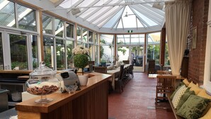 A conservatory with a wooden reception desk, seating area, and a view of the garden. - CygnetOldBank- Accommodation, Cafe Escape the everyday, style & bliss (Cygnet)