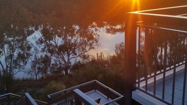 A sunset view from a balcony overlooking a body of water with trees and a distant horizon. - Apartment 37 on Lemon (Mildura)
