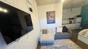 A modern living room with a flat-screen TV, a grey sofa, a patterned rug, and a kitchen area in the background. - Apartment 37 on Lemon (Mildura)
