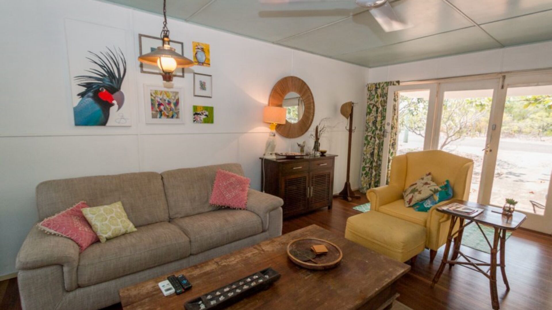 A living room with a sofa, armchair, coffee table, and a lamp. There are wall art pieces and a mirror.