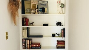 Ein weißes Bücherregal mit verschiedenen Büchern, Dekorationsobjekten und einer kleinen Figur.