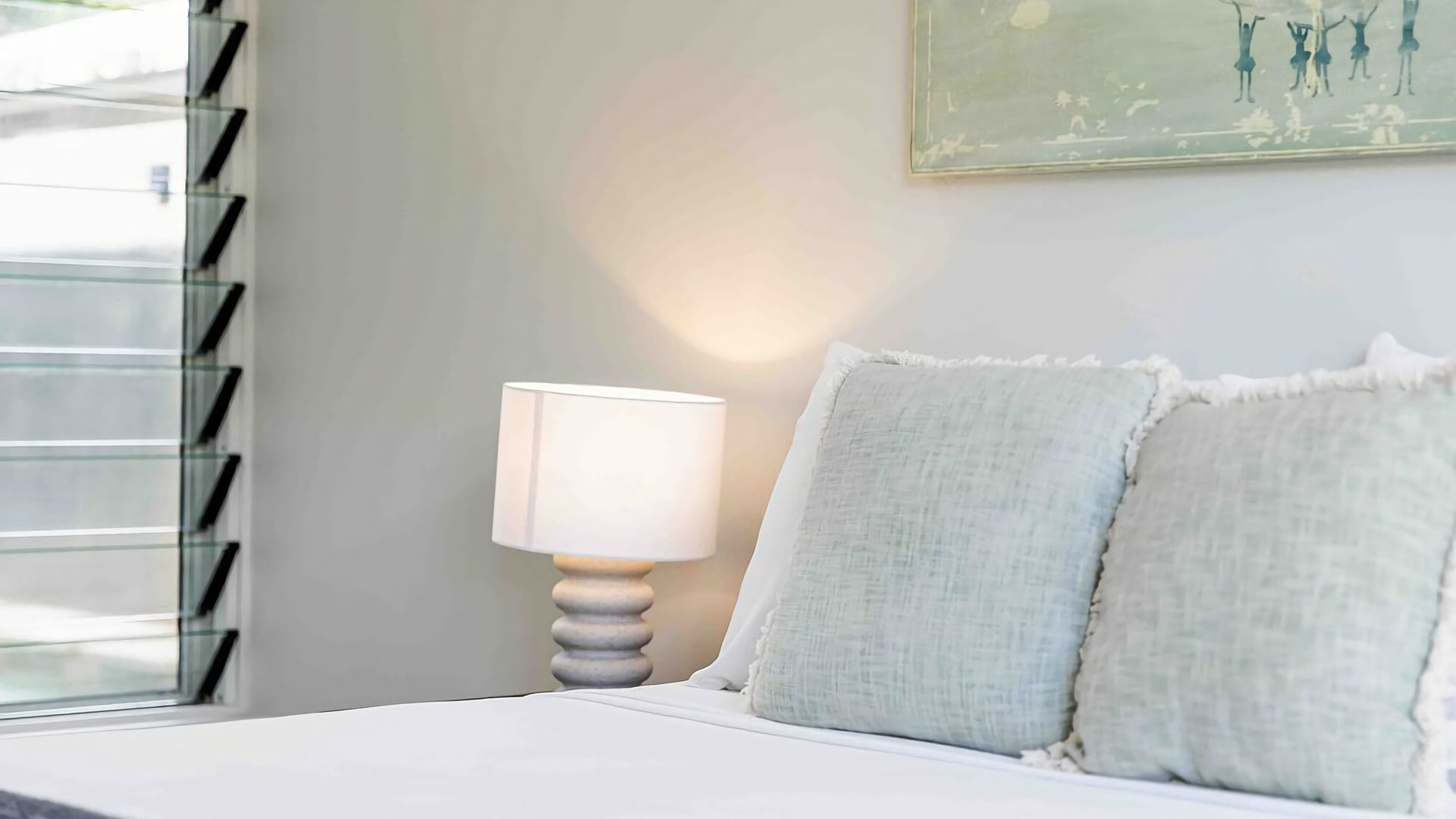 Una camera da letto con un letto, un comodino con una lampada e un quadro appeso al muro.