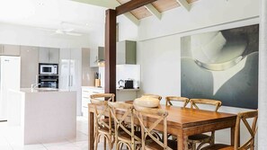 Una cocina moderna con armarios blancos, un comedor con mesa y sillas de madera, y un cuadro abstracto grande en la pared.