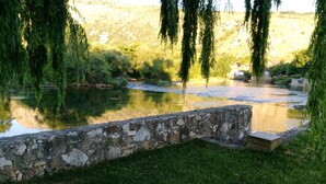 Un muro de piedra con una zona verde al frente, un cuerpo de agua tranquilo y árboles de fondo.