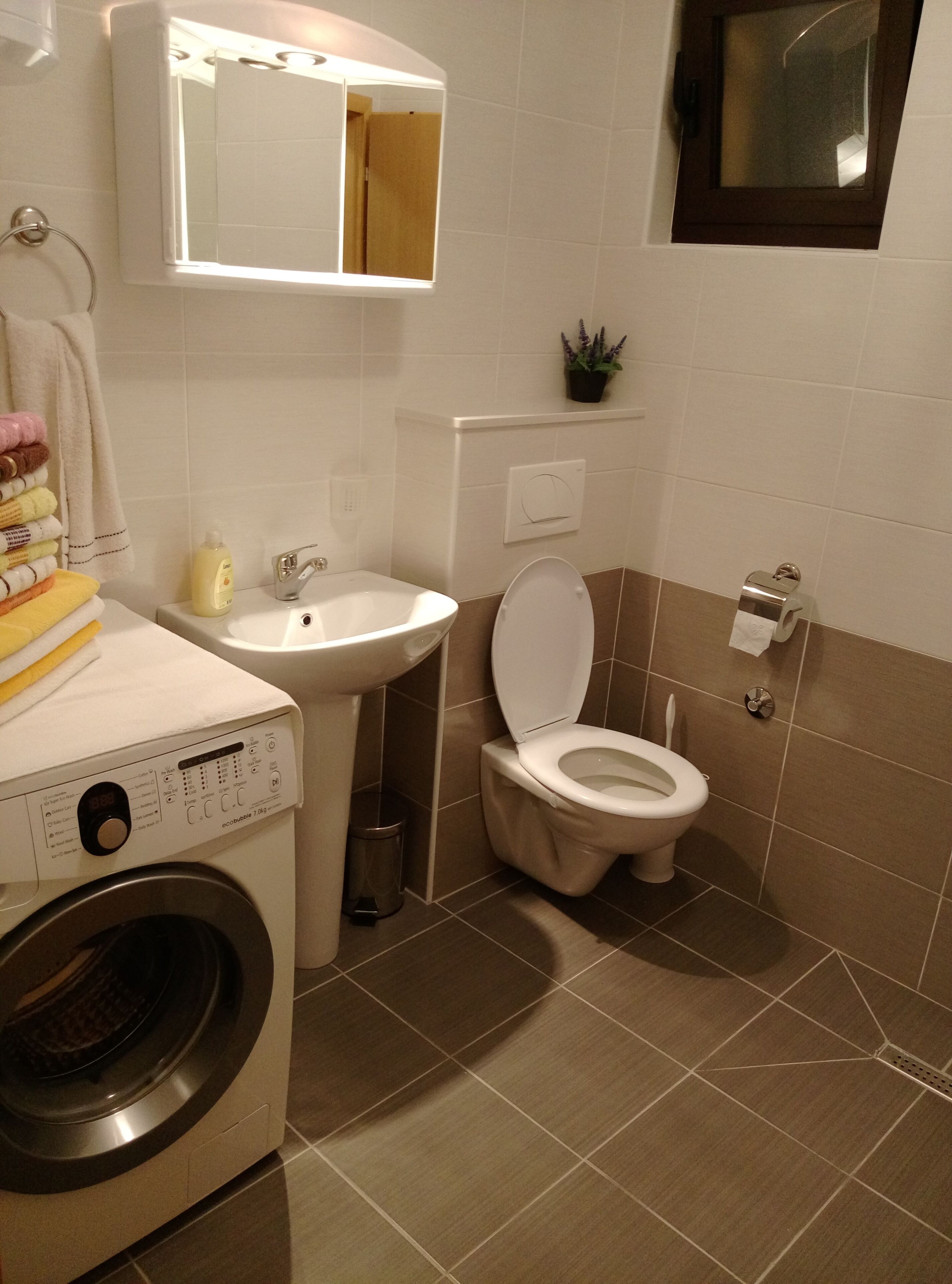 A compact bathroom with a washing machine, a sink, and a toilet.