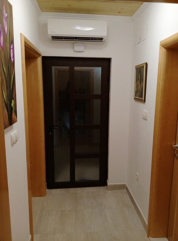 A hallway with a wooden door, an air conditioning unit, a painting, and a light switch.