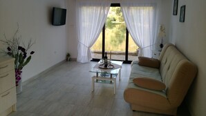 Una sala de estar con un sofá, una mesa de centro de vidrio y un televisor montado en la pared.