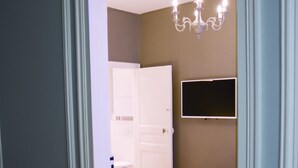 A hotel room with a bed, a chandelier, a television mounted on the wall, and a door leading to another room. - Brand new chic 30 m2 for 4, quite, in the best part of the hypest 9th district (Paris)