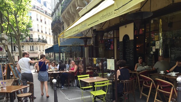 An outdoor cafe with tables and chairs, a yellow awning, and a building in the background. - Brand new chic 30 m2 for 4, quite, in the best part of the hypest 9th district (Paris)
